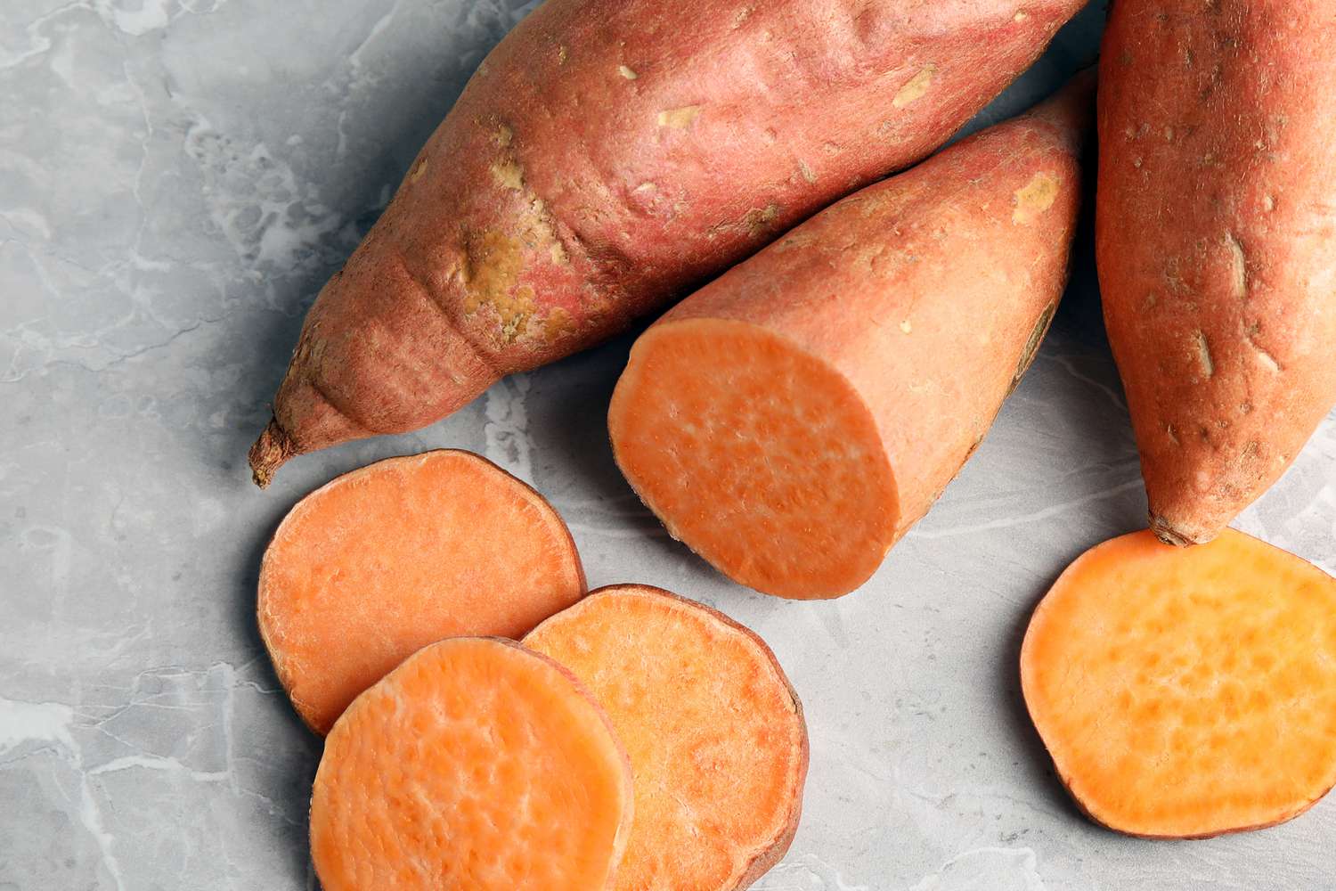 Whole and sliced sweet potatoes on a stone surface