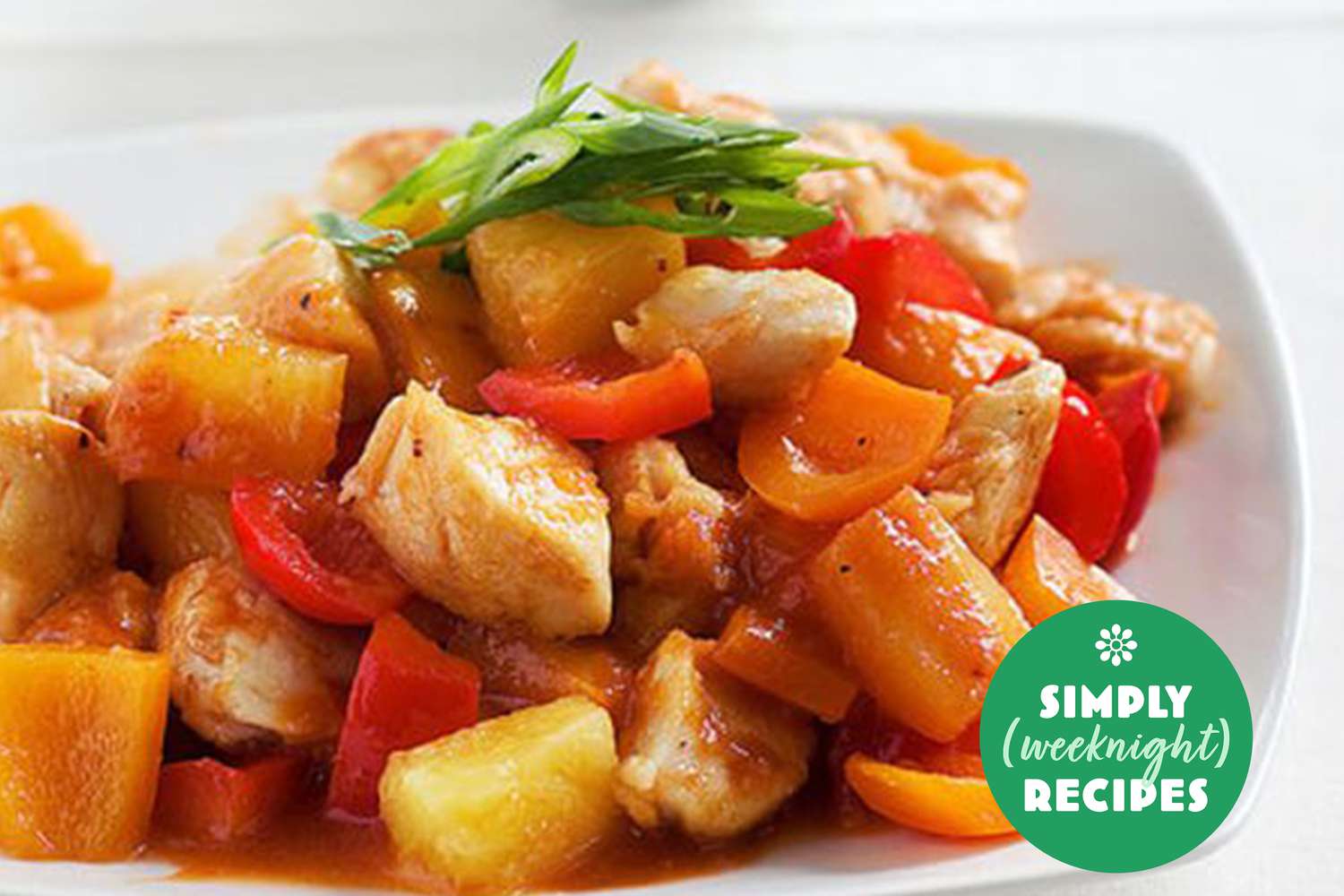 A plate of stir-fried chicken mixed with bell peppers, pineapple chunks, and green garnish