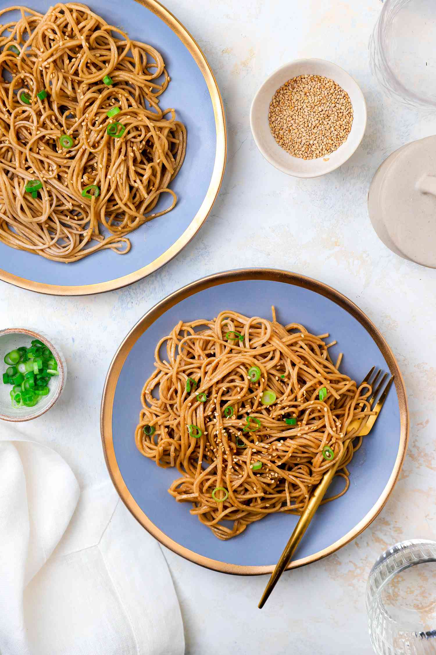 Plates of Sesame Peanut Noodles Next to a Small Bowls of Sesame Seeds and Green Onions