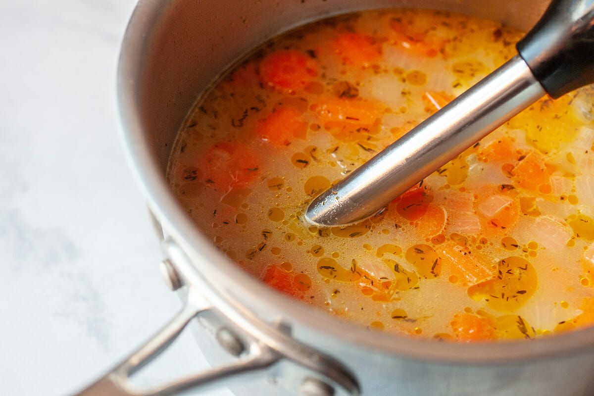 Immersion blender in a pot of carrot soup, blending the ingredients 