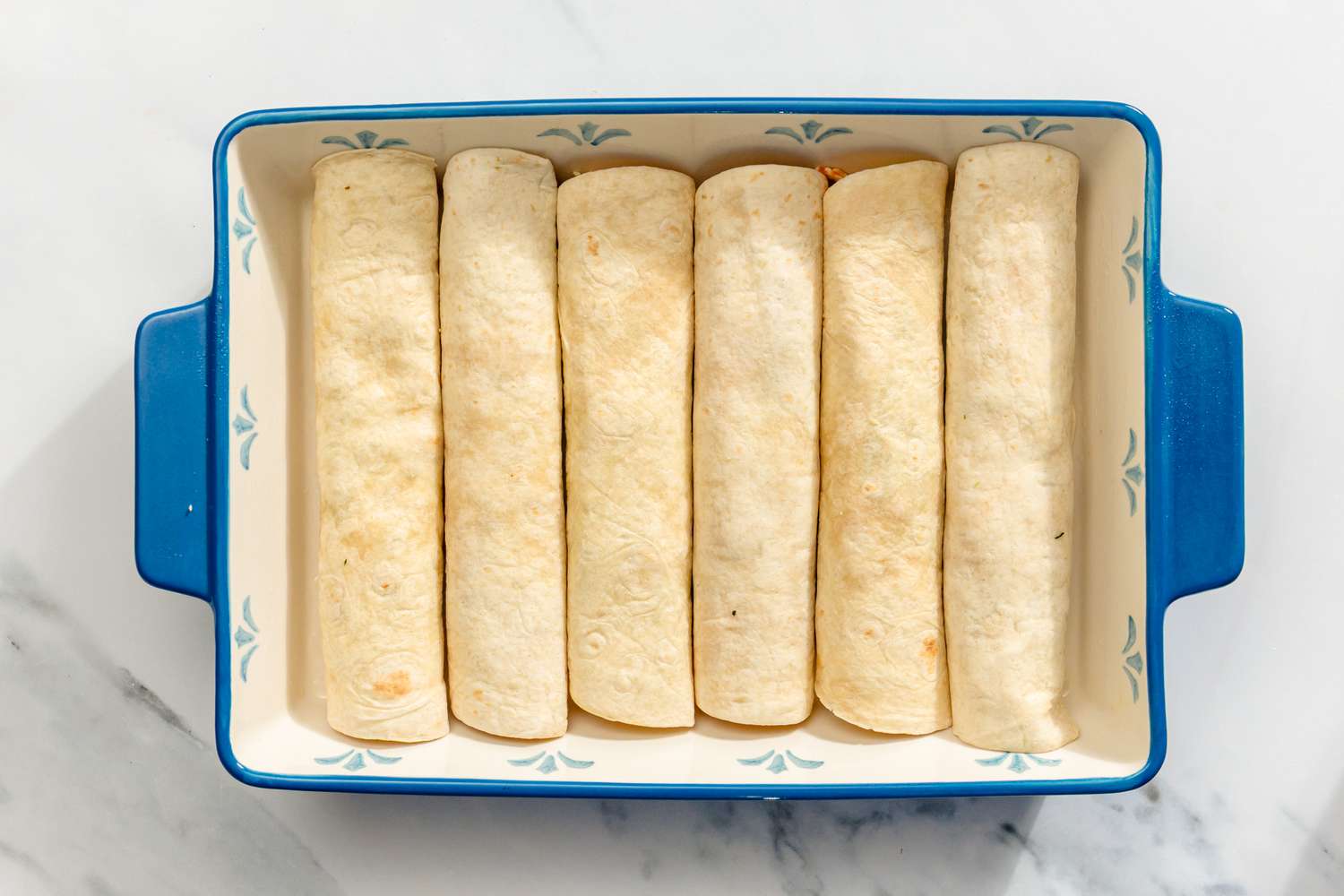 A baking dish containing rolled tortillas arranged side by side for Chicken and Spinach Tortilla Bake recipe