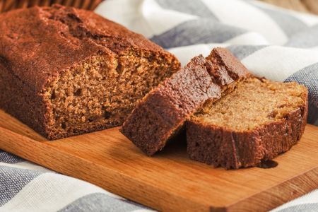A loaf of spice cake on a wooden board partially sliced with two pieces visible