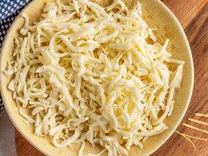 Photo of a bowl of shredded cheese and a blue and white checkered kitchen towel on a wooden tray with yellow illustrations