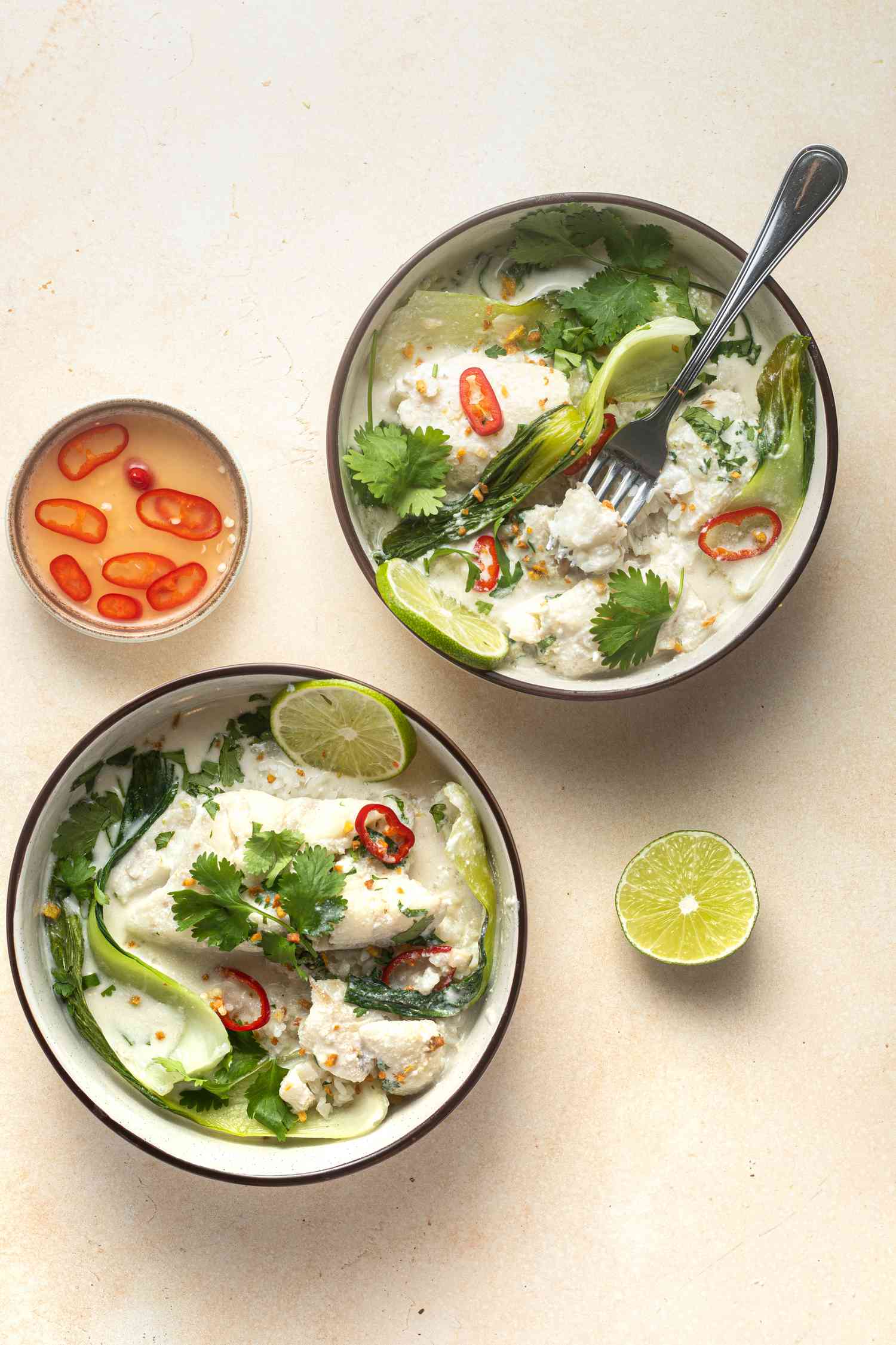 Overhead view of two bowls of Coconut poached cod with ginger and lime served with lime and rice.