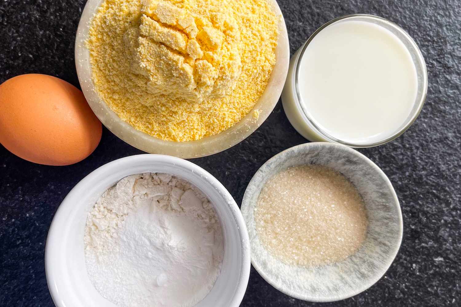 Cornmeal milk egg sugar and flour in bowls ingredients for cornbread preparation
