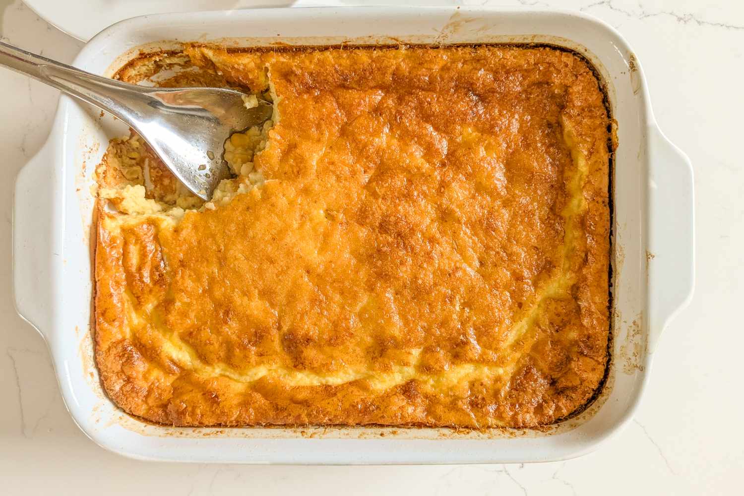 Nigella Lawson's Sweet Corn Pudding in a casserole dish with a large serving spoon