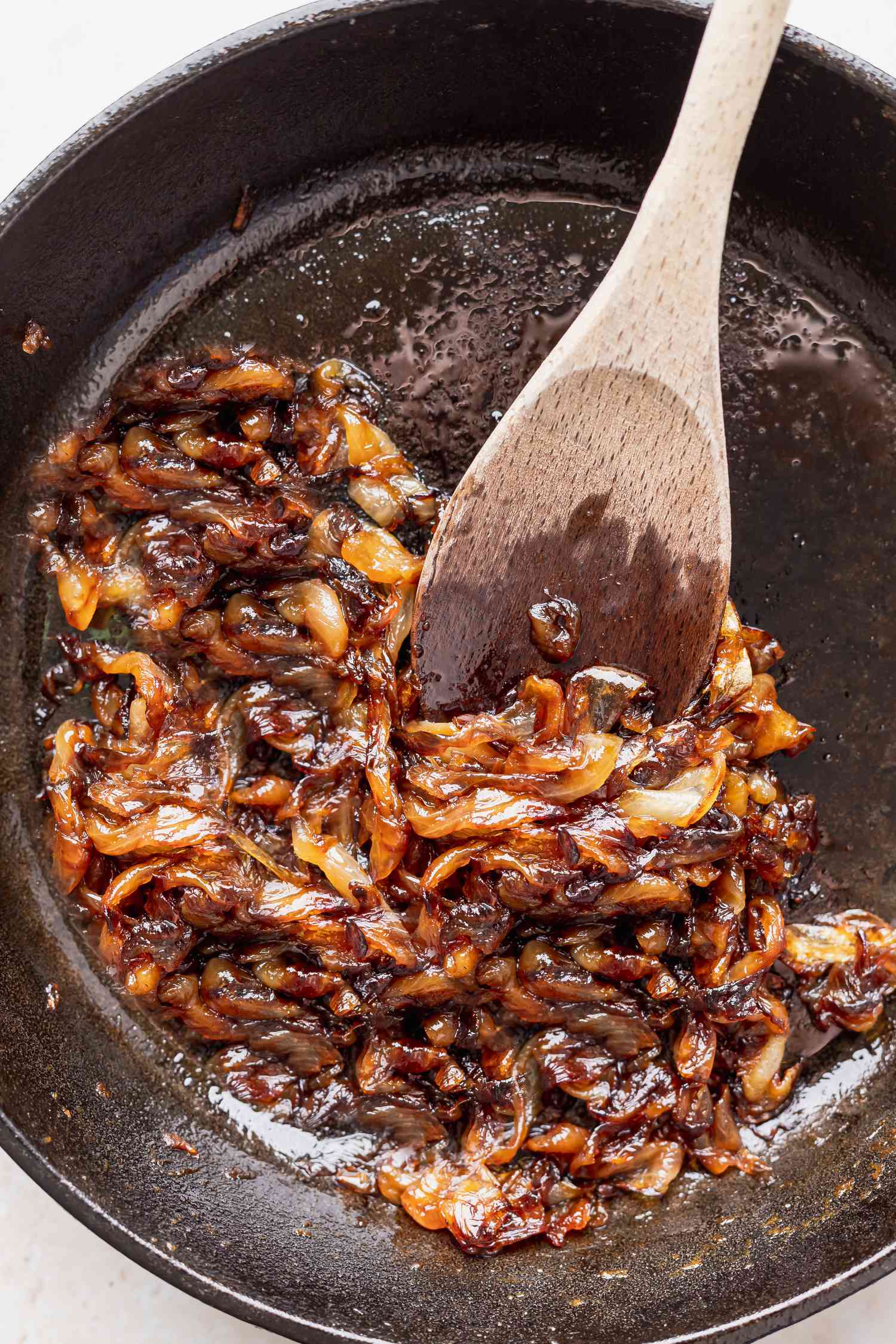Caramelized onions being stirred with a wooden spoon in a cast iron skillet