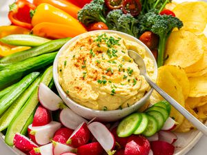 Closeup view of a platter with vegetables and potato chips arranged around a bowl of deviled egg dip all on a white background