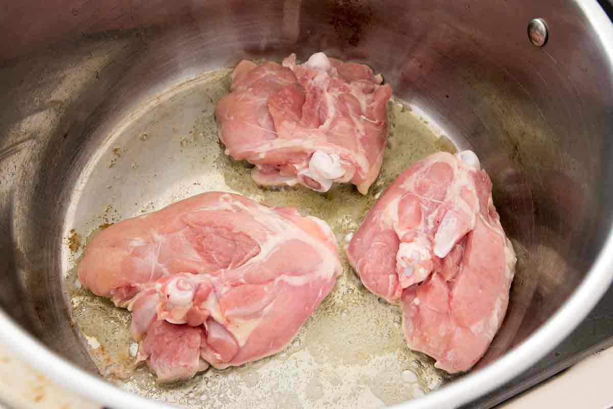 Chicken thighs skin side down in a stock pot for chicken dumplings.