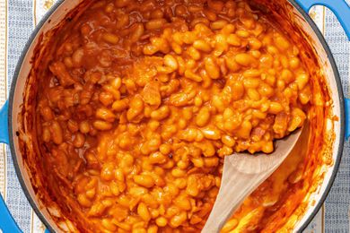Cooked baked beans with a wooden spoon in a pot