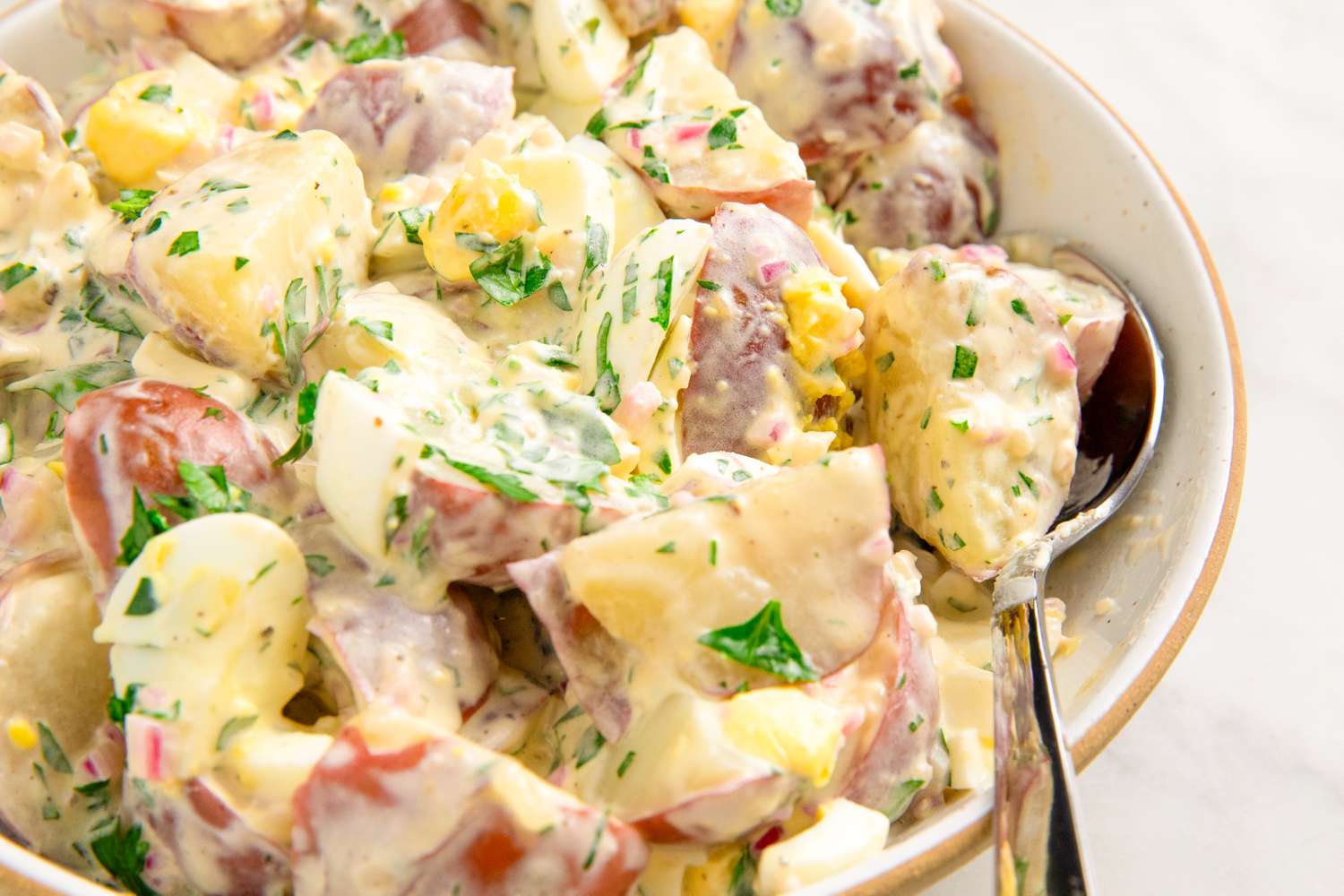 Potato salad with egg and parsley in a bowl served with a spoon