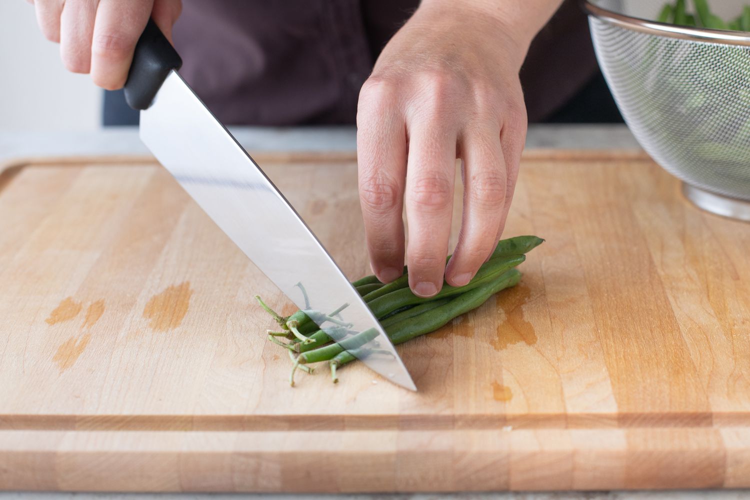 Hand holding chef's knife trimming ends off green beans
