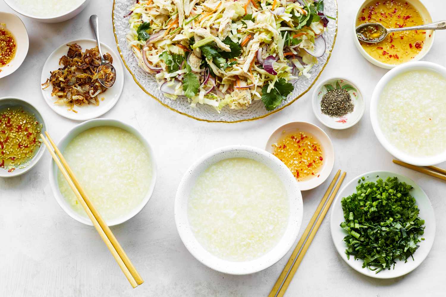 Chào Gá (Vietnamese Rice Porridge) in a Bowl Surrounded by Platter of Vegetables and Bowls of Sauce