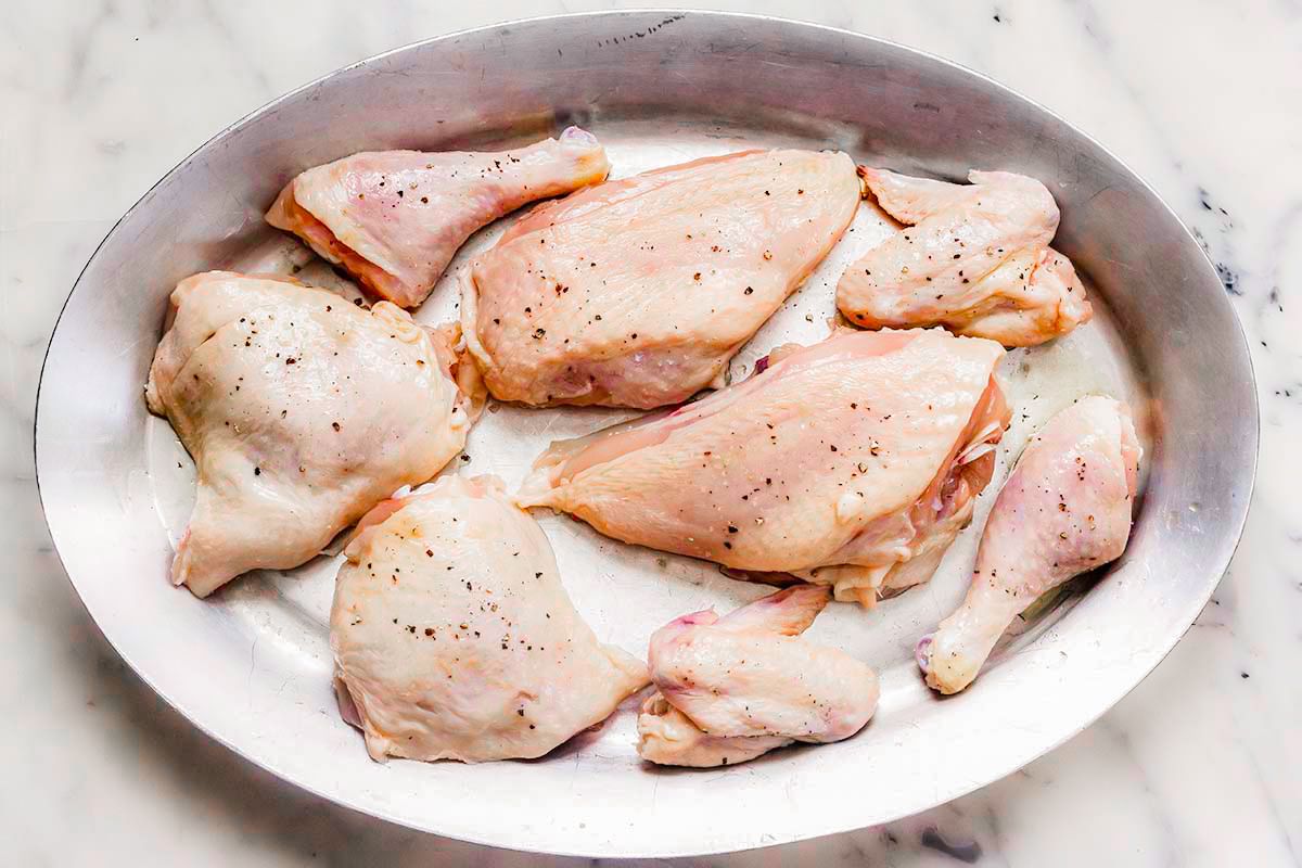 Platter of raw chicken breasts, legs, thighs and wings on a marble countertop