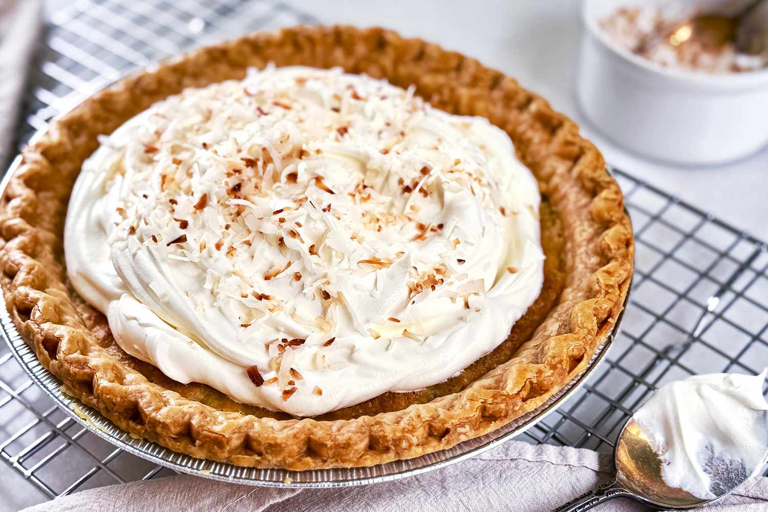 A buttermilk coconut pie topped with whipped cream and toasted coconut on a cooling rack