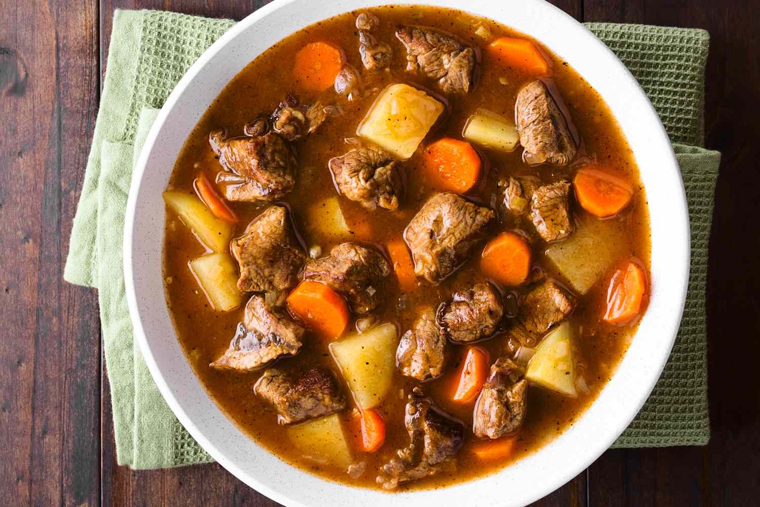 A bowl of beef stew from overhead, showing a rich broth, chunks of beef and potatoes, and rounds of carrot