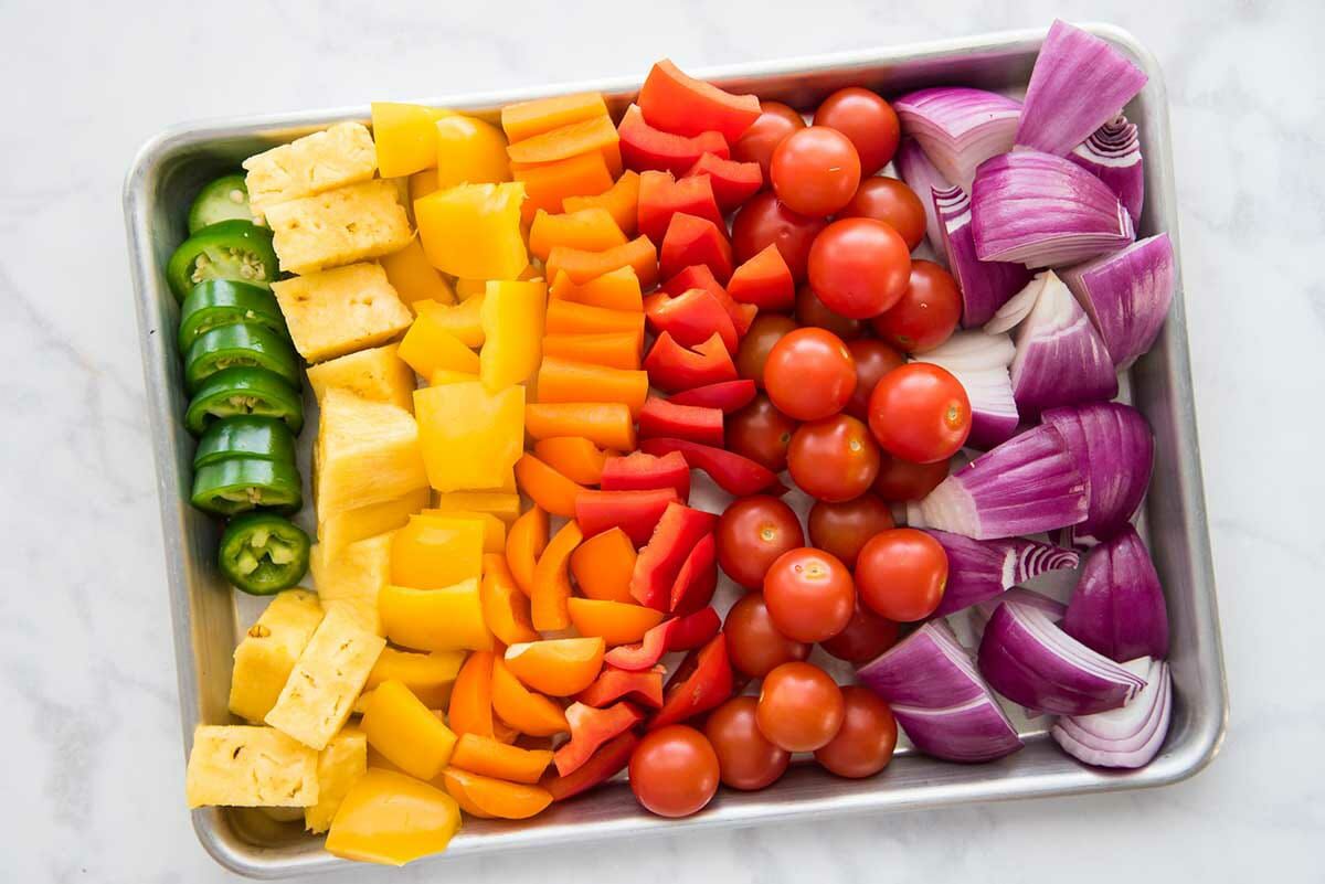 A rainbow of chopped vegetables are lined up on a quarter sheet pan to make easy grilled pork kebabs with mojo marinade.