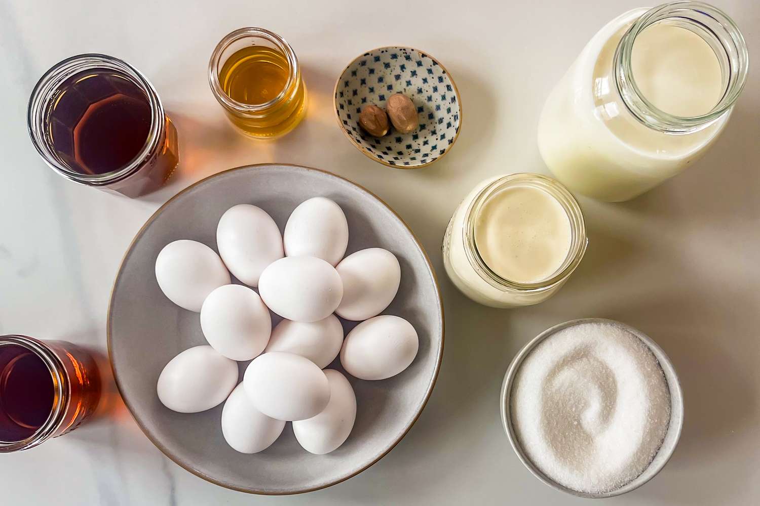 Ingredients arranged for making eggnog including eggs milk cream sugar nutmeg and bottles of rum and other liquids
