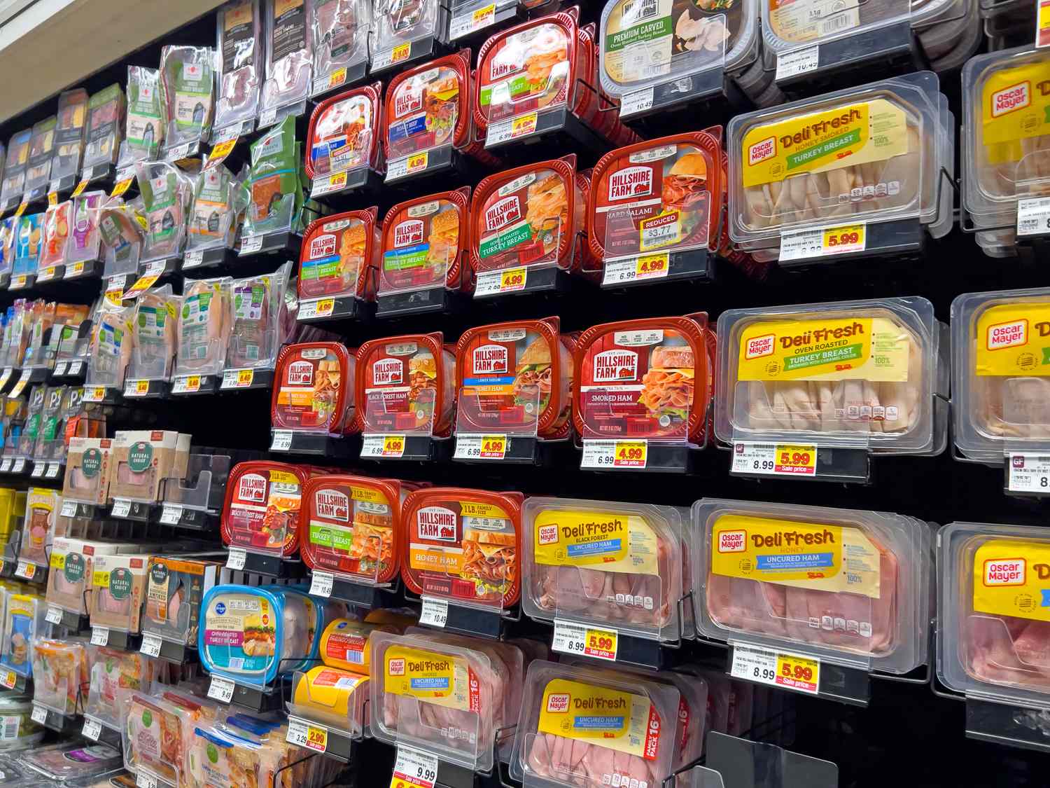 Shelves stocked with various packages of delisliced turkey from different brands in a grocery store