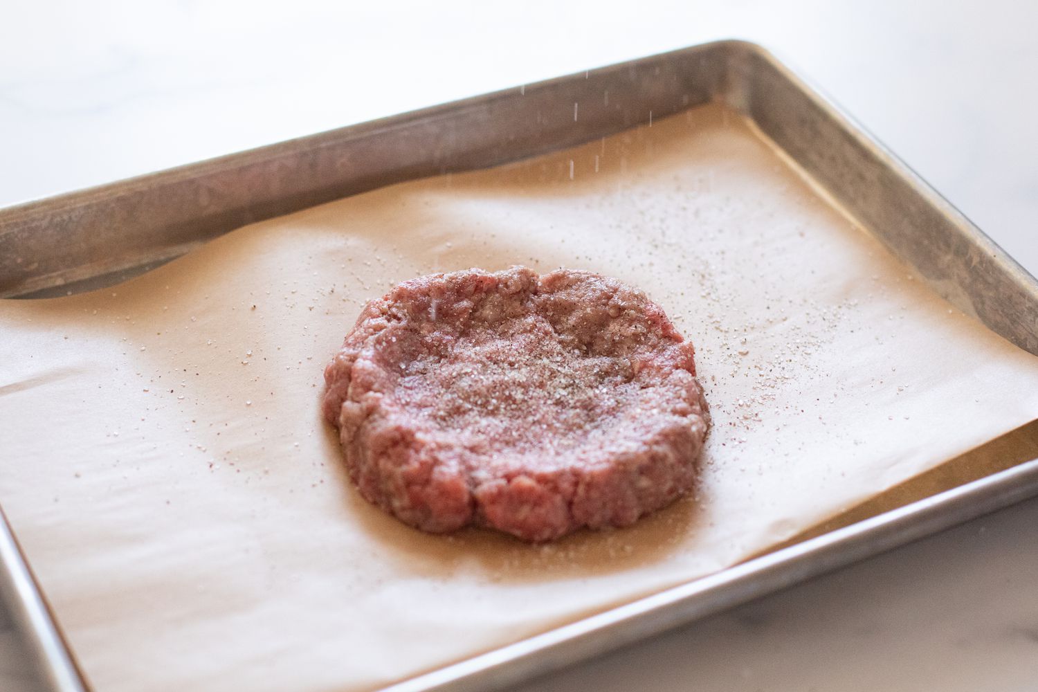 A burger patty on a parchment lined baking sheet to show the best way to season a burger.