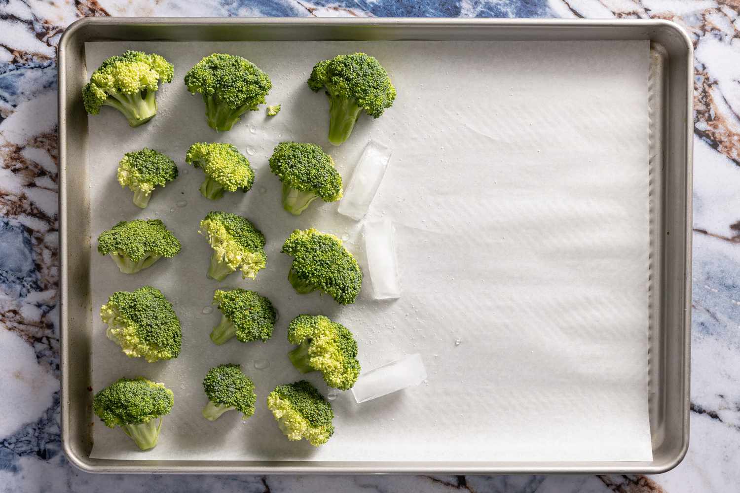 broccoli and three ice cubes on a parchment paper lined baking tray for crispy parmesan broccoli recipe