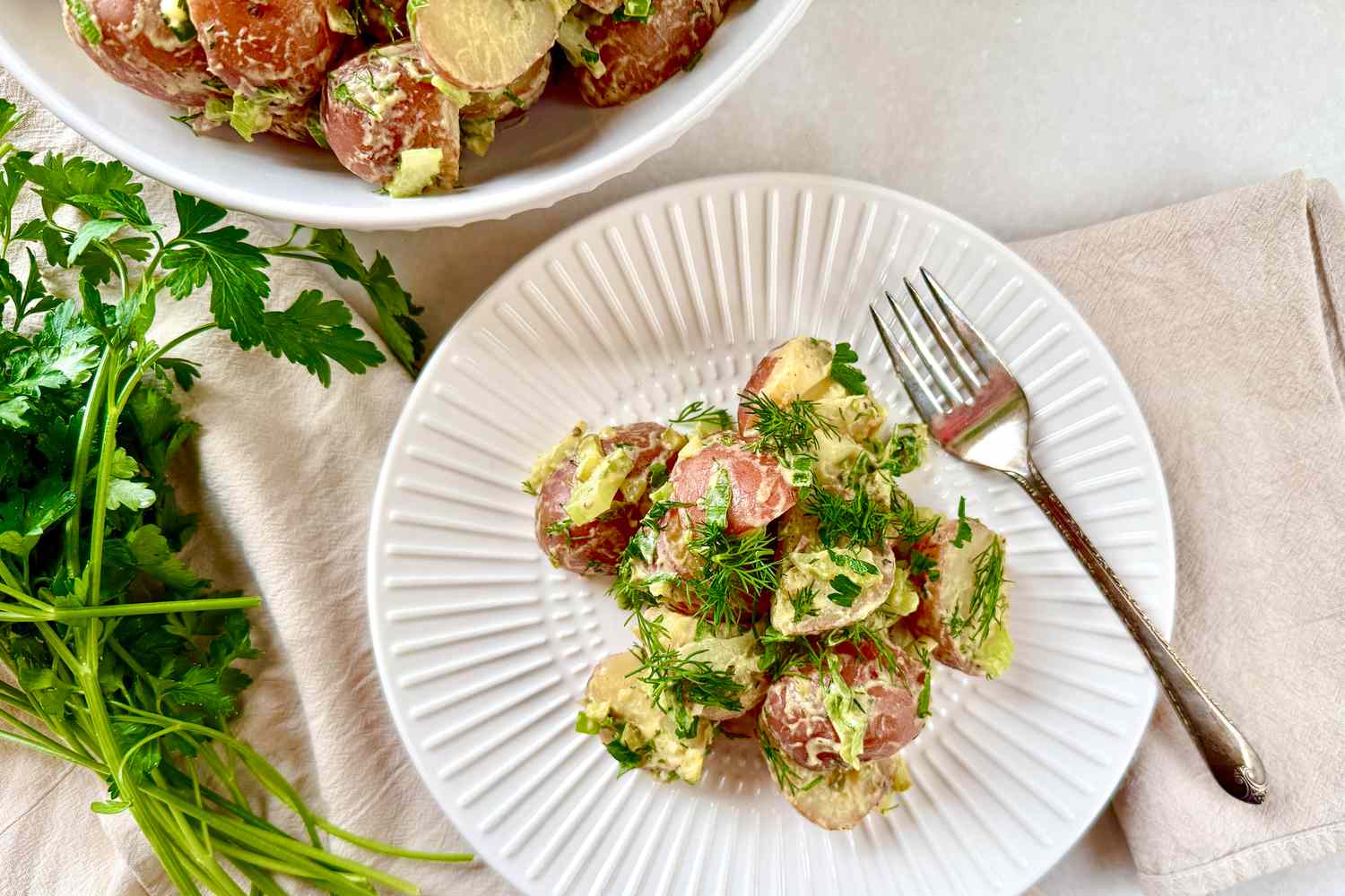 Potato salad on a white plate with a fork and a bowl with more potato salad on the side