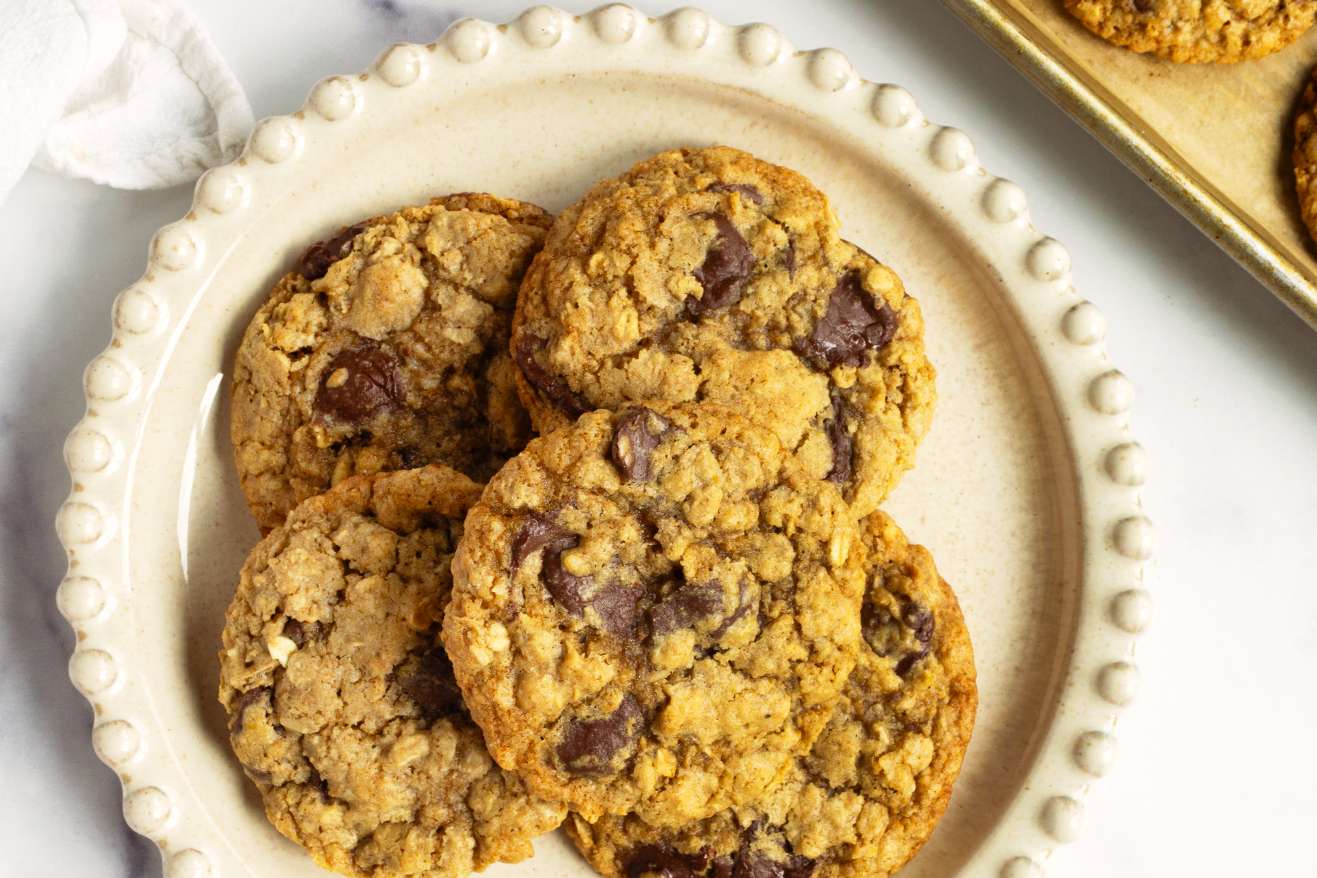 A plate of oatmeal chocolate chip cookies and a baking tray with more cookies