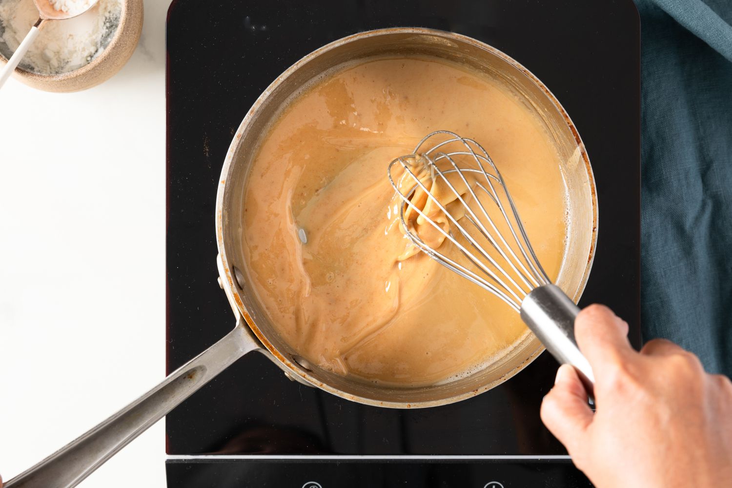 Roux whisked until blond roux is made (in pot on a portable stovetop next to a bowl of flour and a blue kitchen towel) for how to make roux, with recipe