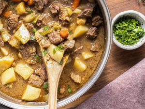 Pot of Easy Beef Stew with a Wooden Spatula, a Small Bowl of Parsley, a Sprig of Thyme, and a Kitchen Towel