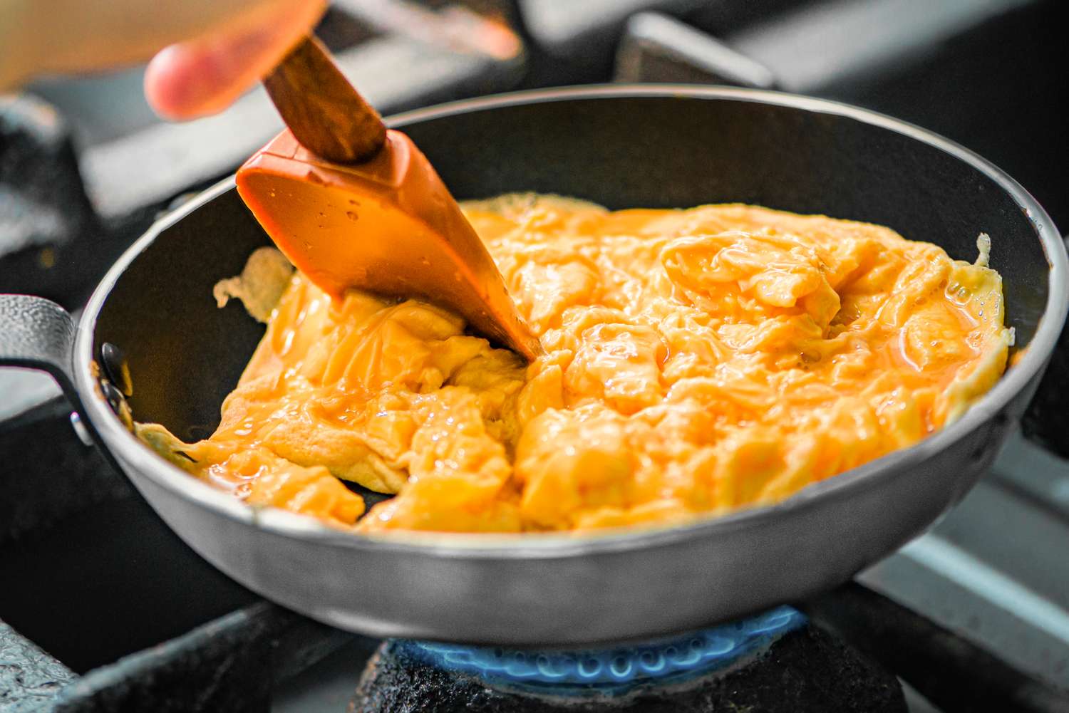 Scrambled eggs being stirred in a pan with a spatula over a flame