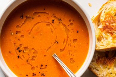 A bowl of soup topped with a drizzle of oil with toasted bread slices on the side