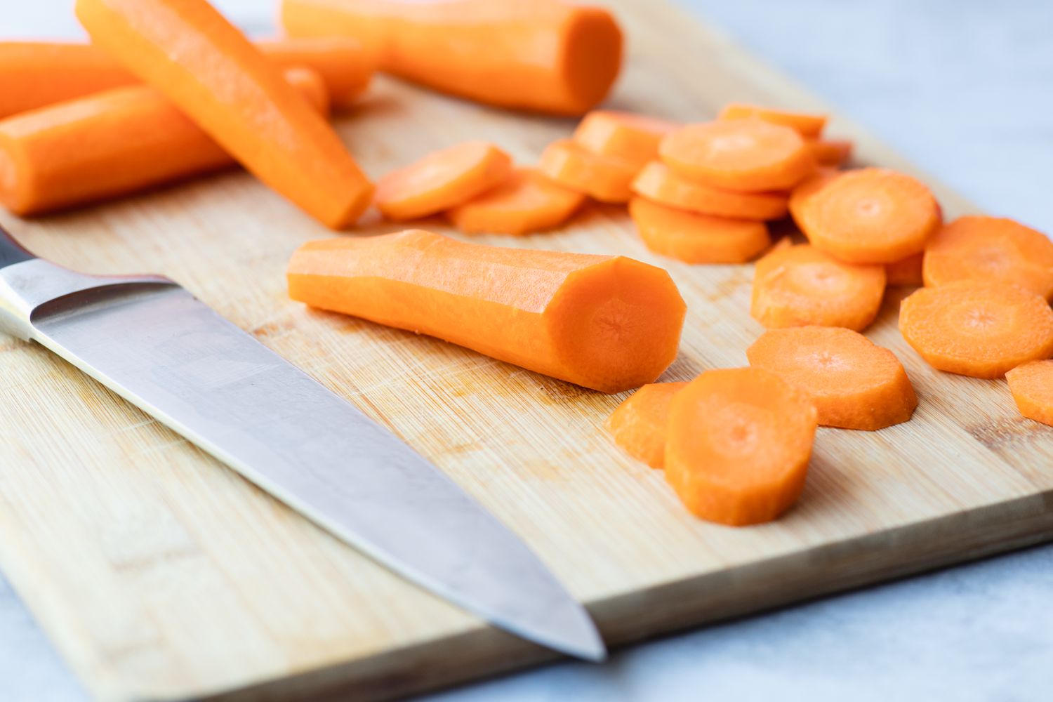 Cutting board with carrots being sliced for a glazed carrots recipe.