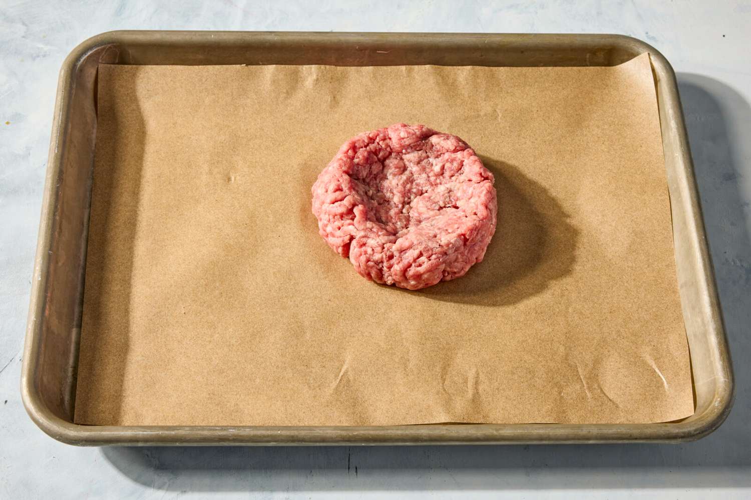 Burger patty with an indented center on parchment-lined baking sheet