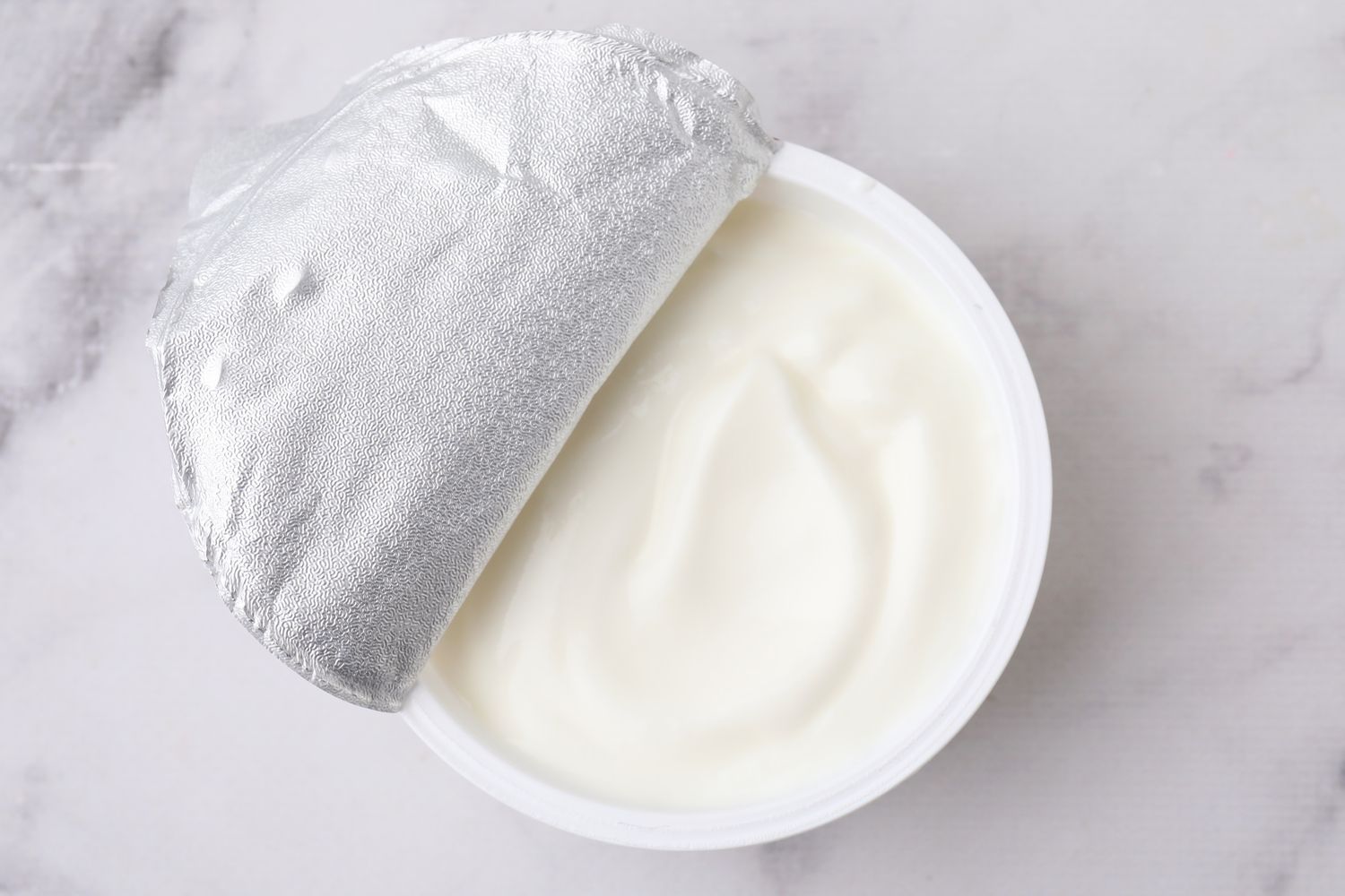 An opened container of yogurt with its foil lid partially peeled back