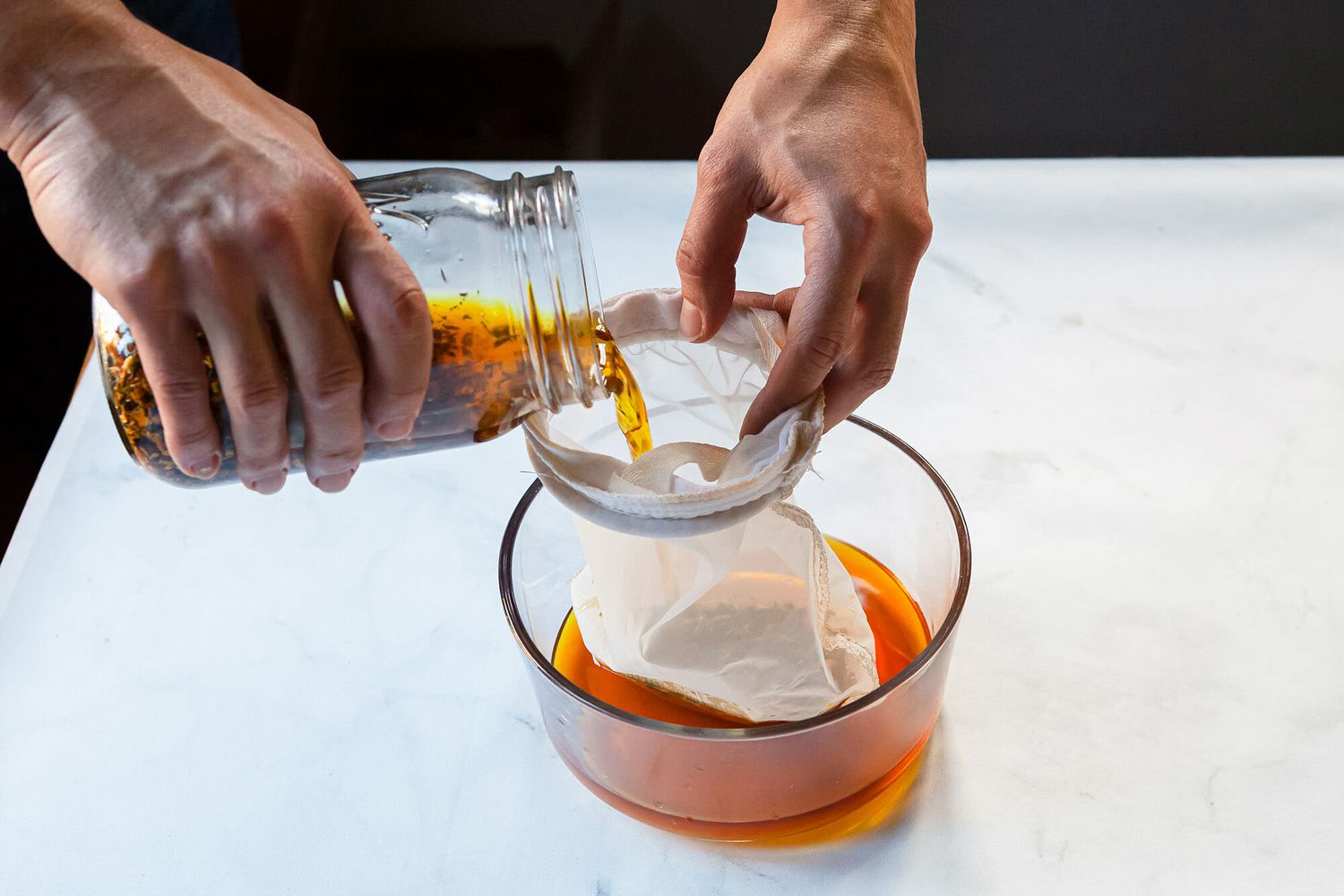 A person pouring ingredients for campari through a mesh bag and into a glass bowl.