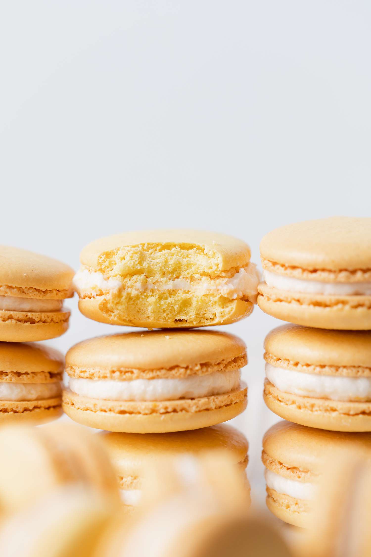 Side view ofFrench macarons with lemon buttercream filling in three stacks with the middle one with a bite out of it.
