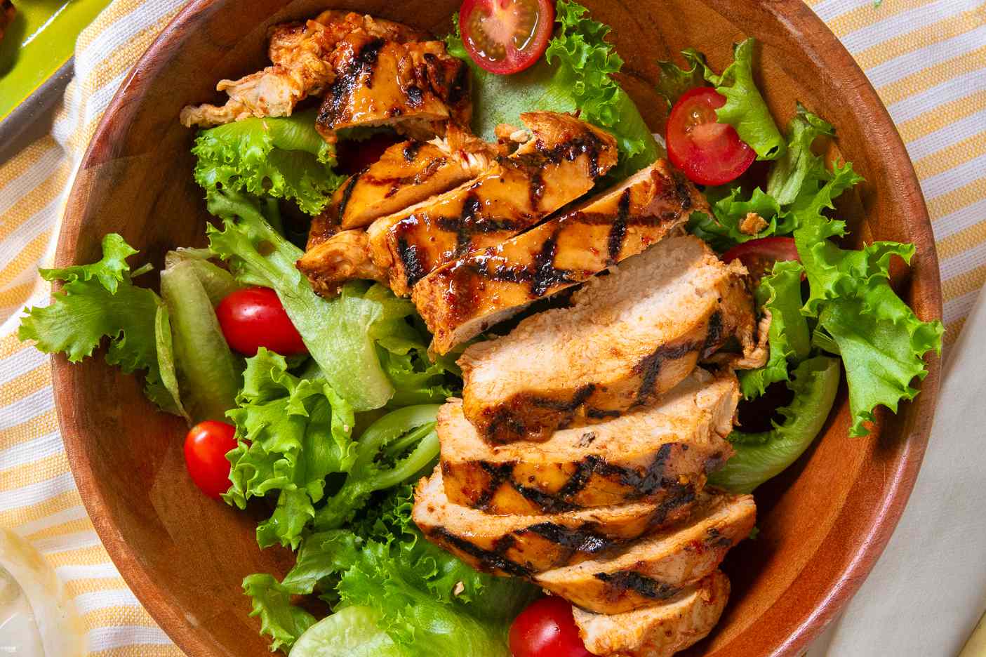 sliced grilled chicken over a bed of salad greens and halved cherry tomatoes in a bowl
