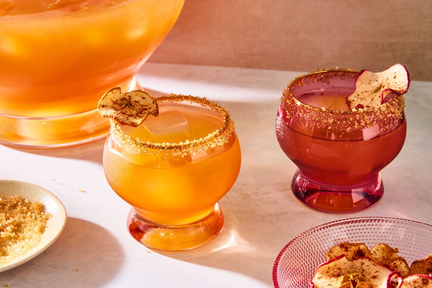 Two glasses of whiskey cider punch garnished with dried apple slices with a punch bowl in the background