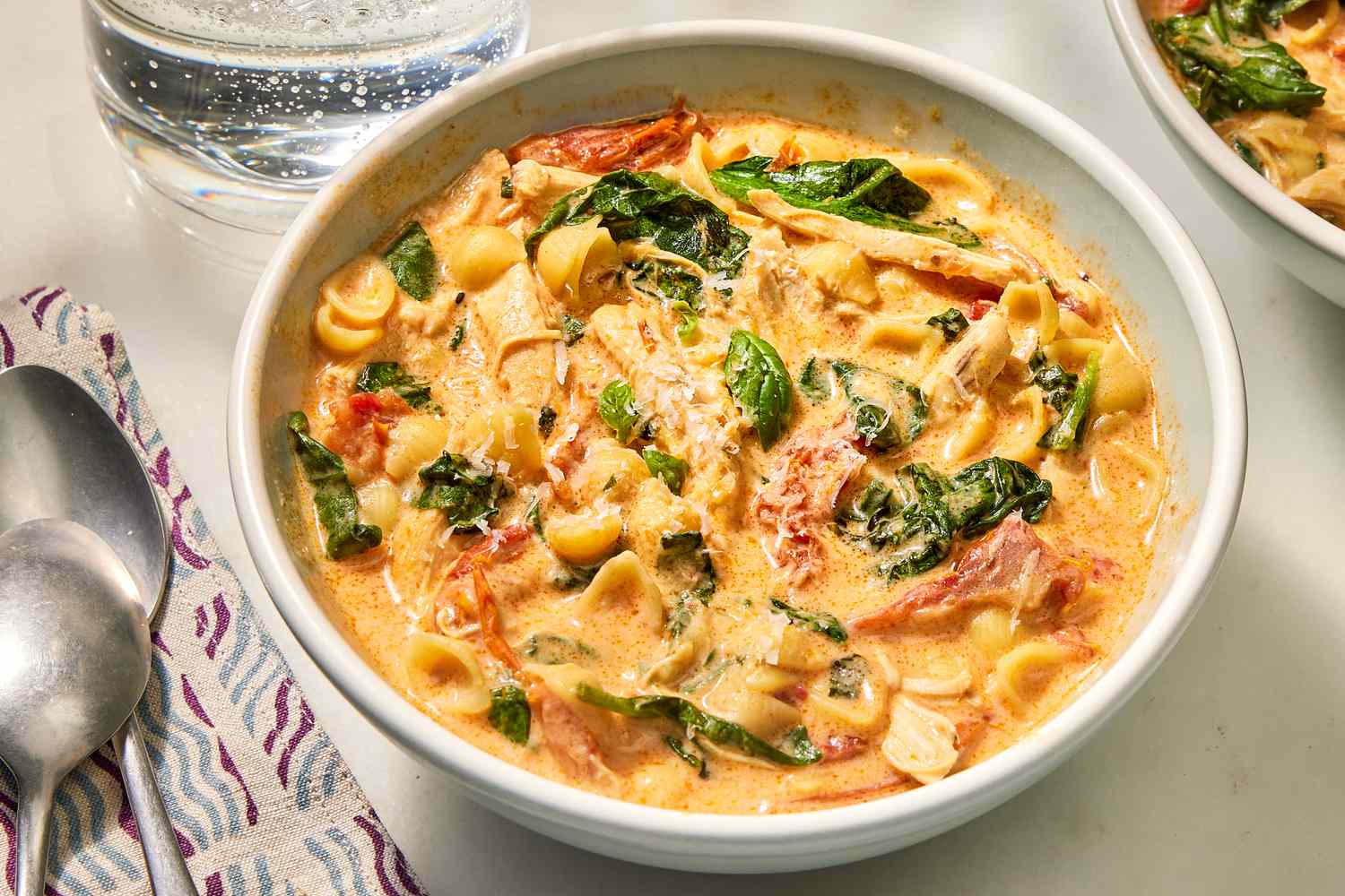 Overhead view of a white bowl of Marry Me Chicken Soup with a two spoons and a napkin to the left