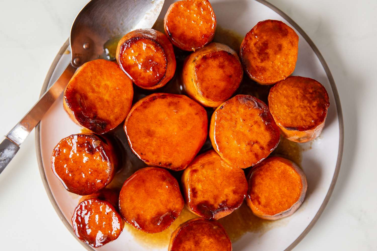 A plate of glazed sweet potato rounds served with a spoon