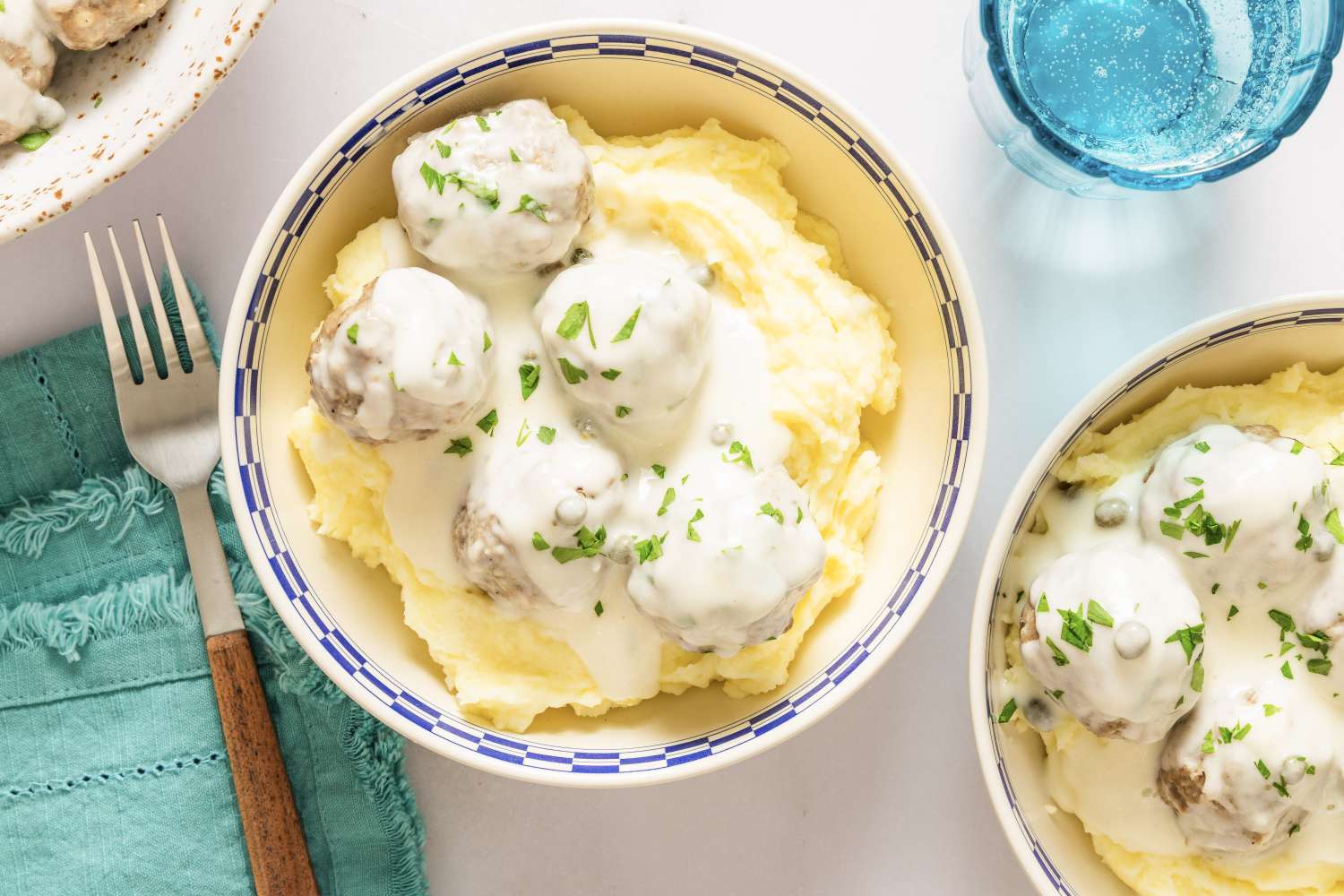 A bowl of Konigsberger Klopse served on mashed potatoes garnished with sauce and herbs