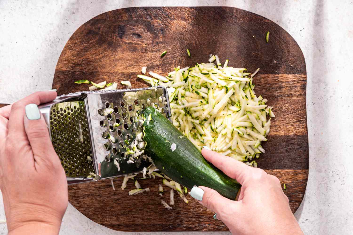 Zucchini Grated Using a Box Grater Over a Wood Cutting Board for Zucchini Butter Recipe