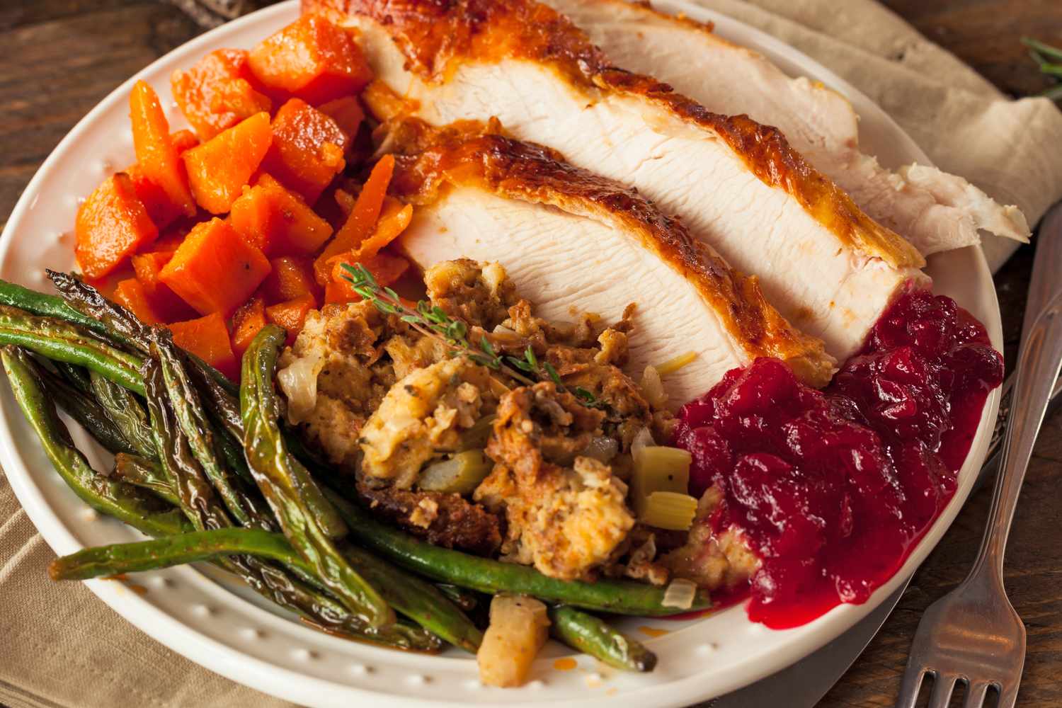 A plate with Thanksgiving dinner including slices of turkey stuffing cranberry sauce roasted carrots and green beans