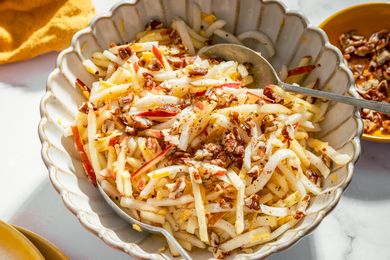 Kohlrabi and apple salad garnished with chopped nuts in a serving dish with a spoon