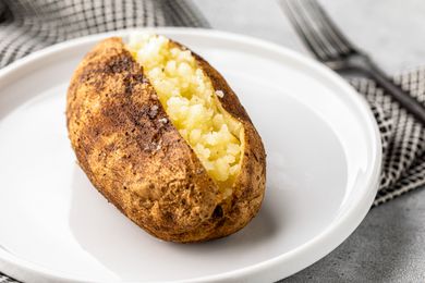 Opened Grilled Baked Potato on a Plate Next to a Fork and Napkin