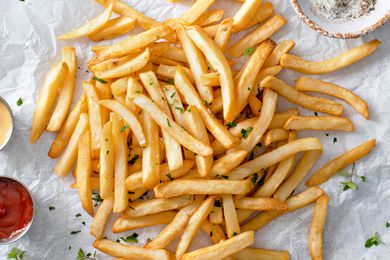 A serving of French fries on parchment paper garnished with parsley and accompanied by dipping sauces
