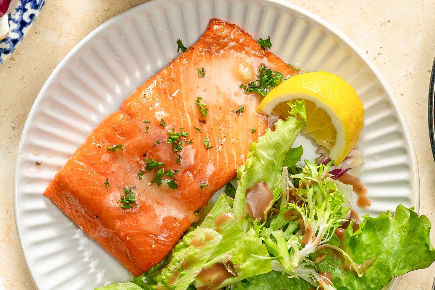 Closeup overhead shot of a roasted salmon fillet next to a green salad and a lemon slice on a plate