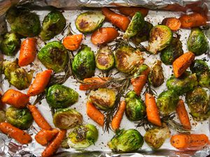Overhead view of roasted brussels sprouts with rosemary and carrots on a baking sheet lined with foil