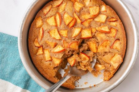 Apple spoon cake in a round baking dish with a portion served using a spoon