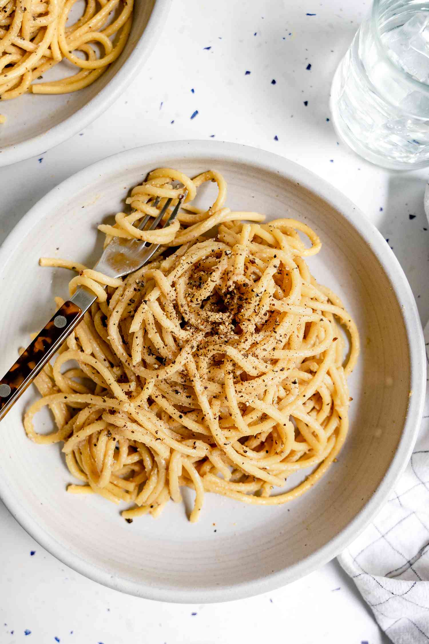 Vegan Cacio e Pepe Topped with Cracked Pepper on Plate with Some of Pasta Wrapped around a Fork